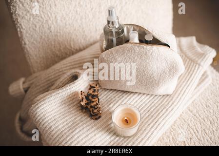 Fluffy cosmetic bag with make up cosmetic products on knitted clothes in chair closeup top view. Stock Photo