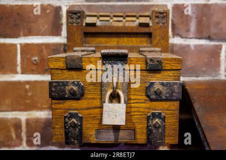 Wooden collection box padlocked attached to brick wall in a church Stock Photo