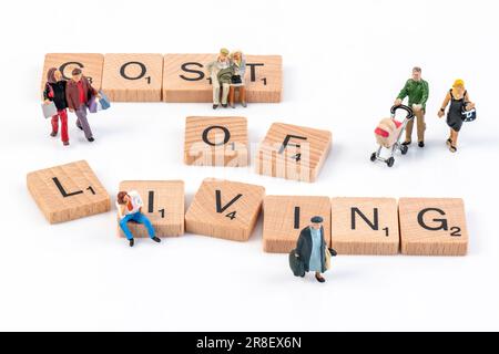 Cost of Living - Wooden Scrabble letters arranged to spell 'Cost of Living' surrounded by small figurines depicting various age groups. Stock Photo