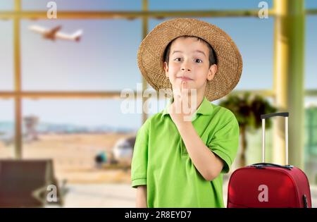 Dark haired boy wearing green t-shirt and hat at airport with hand on chin thinking about question, thoughtful expression. Smiling with thoughtful fac Stock Photo