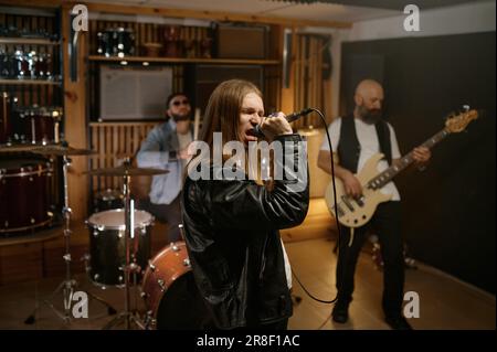 Stylish vocalist with long hair emotionally singing song into microphone Stock Photo