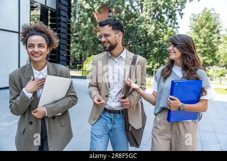 Quick briefing before meeting. Group of cheerful young successful business people talking to each other while walking outdoors. Office workers experts Stock Photo