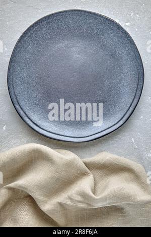 empty handmade blue ceramic plate and beige rough linen napkin on gray concrete table. background for food menu. top view with copy space Stock Photo