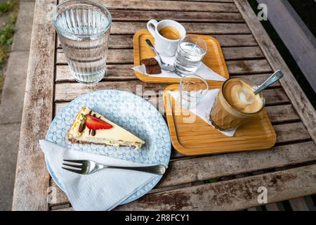 Cheesecake, two coffee and water on small tray on wooden table in garden. Stock Photo