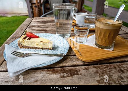 Cheesecake, two coffee and water on wooden table in garden. Stock Photo