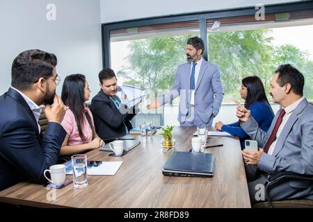 Angry indian boss screaming at male employee for bad work, Businessman ceo scolding incompetent manager blaming and throwing papers at his face for mi Stock Photo