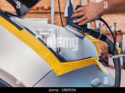 Car polishing service - car cleaner specialist polishing headlamp with polish machine in workshop garage Stock Photo