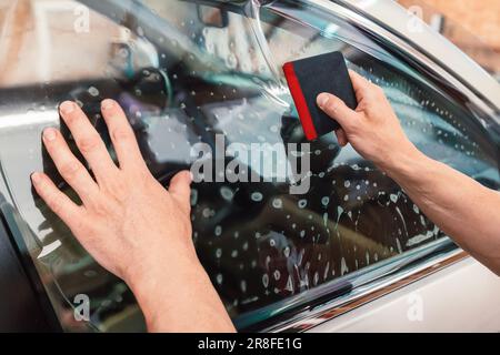 Car tinting windows - Worker specialist applying tint foil on car window Stock Photo