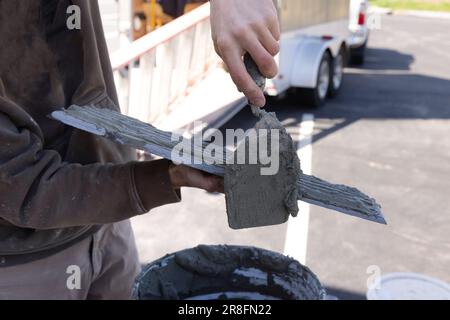 Worker uses trowels to spread wet cement adhesive before installing tiles Stock Photo