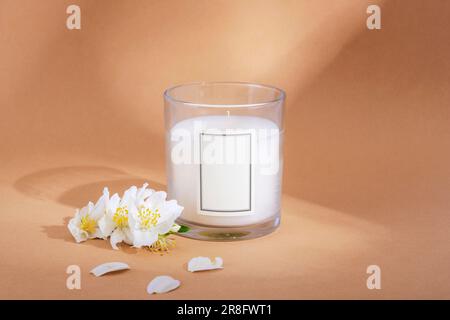 White aroma candle and jasmine flowers on beige background with light and shadows. Closeup. Stock Photo