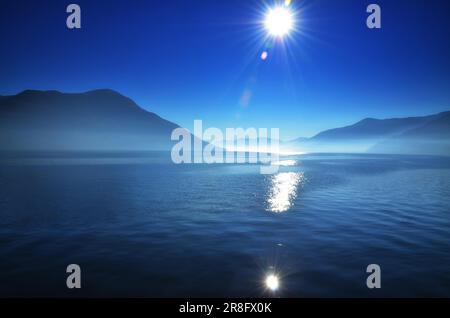 Foggy Alpine lake Maggiore with Sunbeam and Mountain in Ticino, Switzerland Stock Photo