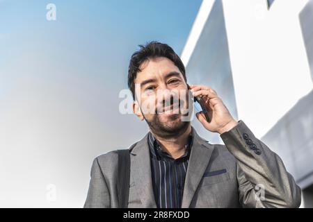 Low-angle view of an attractive businessman talking on the cell phone while looking at camera in the street Stock Photo
