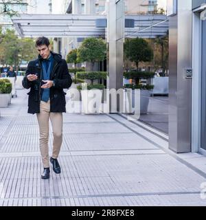 A serious businessman reading a message on his smartphone while walking in the street near his office Stock Photo