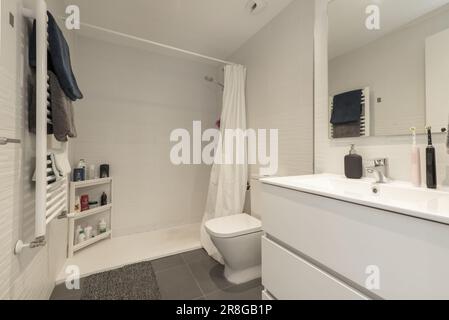 Simple modern bathroom with walk-in shower, frameless mirror on the wall, white heated towel rail and white wooden hanging cabinet Stock Photo