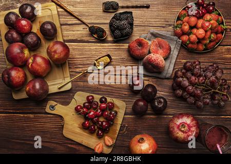 Still life with ripe dark red fruit with plums, nectarines, umbrellas, forest fruits, grapes and red pomegranates Stock Photo