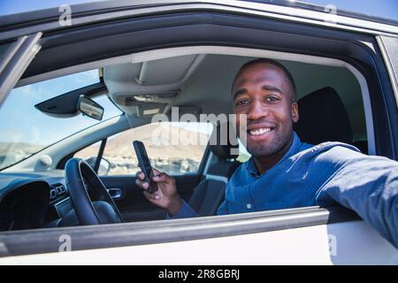 A smiling businessman sitting in his car takes a selfie while using his smartphone Stock Photo
