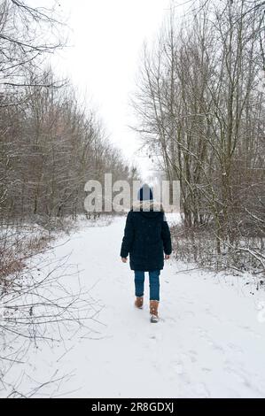 woman with knitted hat and coat, walking along a path covered in snow, winter forest Stock Photo