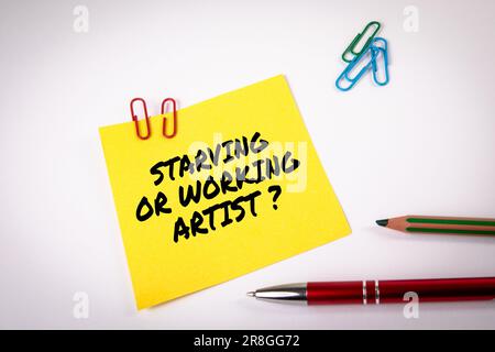 Starving or working artist. Yellow sticky note with text on a white background. Stock Photo