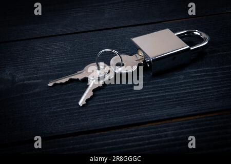 Padlock with three keys on dark wood texture background. Stock Photo