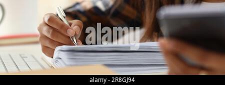 Woman writes hand on agenda while consulting mobile phone on desk at home or in office Stock Photo