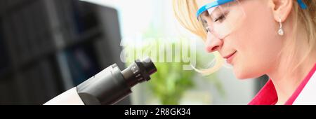 Woman scientist in glasses conducts research through microscope in chemical laboratory Stock Photo