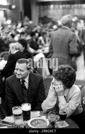 Couple drinking together Saturday night out. 1980s UK. Their bingo cards are on the table. Their is a large metal ashtray. He is wearing his best clothes, suit and tie and has brylcreamed and polished back his hair he has a very low side parting. Coventry, England circa 1981. 80s HOMER SYKES Stock Photo