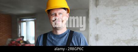Joyful handyman, builder in uniform and hard hat looks at camera and takes notes on clipboard Stock Photo