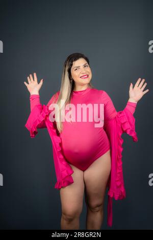 A happy pregnant Caucasian woman posing in a pink bodysuit and robe for a maternity shoot Stock Photo