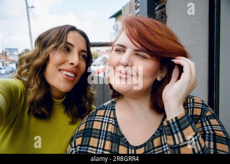 Selfie portrait of two Latina friends of Argentinian ethnicity, sitting outdoors, happily looking at each other with love and affection. Stock Photo
