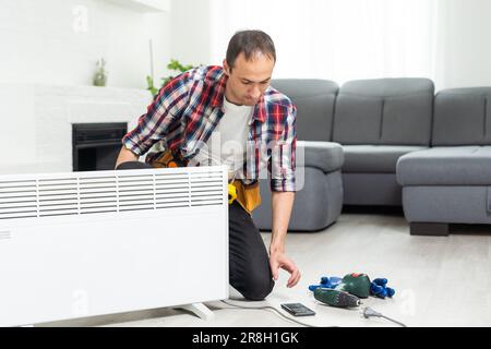 Workman mounting water heating radiator near the window in the white renovated living room, Image with copy space Stock Photo