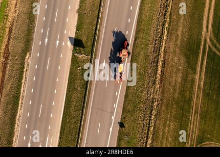 Drone photography of tractor with agricultural equipment driving on a road during spring day. Stock Photo