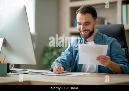 Smiling Young Businessman Working With Papers At Desk In Office Stock Photo