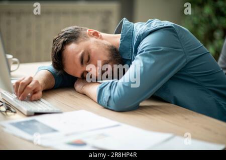 Portrait Of Tired Young Office Employee Sleeping At Workplace Stock Photo