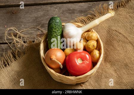 potatoes onions tomato cucumber garlic harvest from the garden lies in a wicker basket on a wooden table, vegetables for the background, vegetable bac Stock Photo