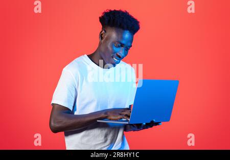 Happy african american man typing on laptop keyboard, red background Stock Photo