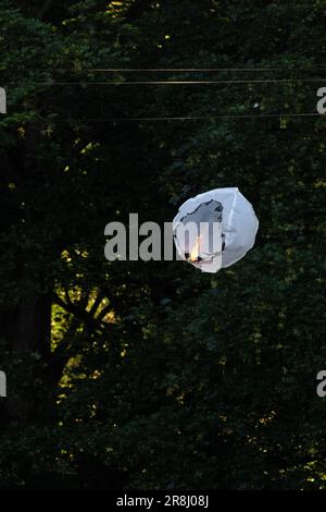 Sky lantern or Chinese lantern alight in the sky - the paper lantern has caught fire and descending next to a tree creating a fire hazard  - UK Stock Photo