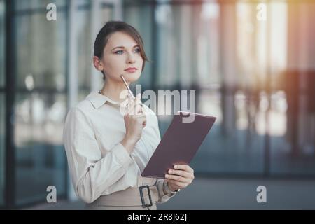 Caucasian business woman with a tablet and a stylus in her hands thought about promising business projects near office building, copy space Stock Photo