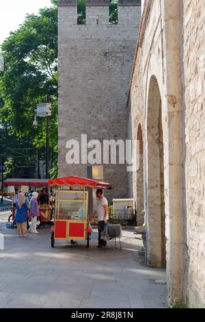 Red Cart selling Simits aka Turkish Bagels by the stone built fortress style entrance Gulhane Park in Istanbul Turkey Stock Photo