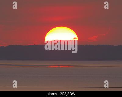 Minster on Sea, Kent, UK. 21st June, 2023. UK Weather: stunning summer solstice sunset as seen from Minster on Sea, Kent. Pic: the sun sets behind Benfleet water tower, Essex. Credit: James Bell/Alamy Live News Stock Photo