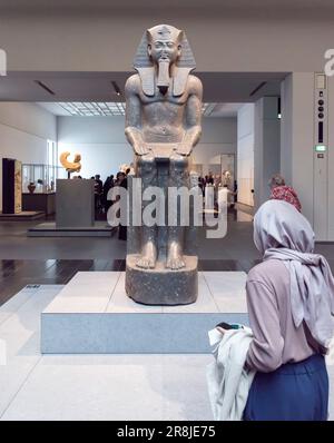 A woman looks at an Ancient Egyptian statue in the Louvre Museum, Abu Dhabi, UAE Stock Photo