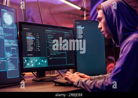 Asian hacker using ransomware to attack server and cracking password. Internet scammer in hood planning phishing attack and developing malicious software to breach data in dark room Stock Photo