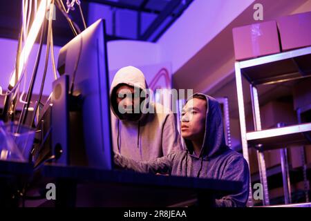 Hackers breaching server and installing illegal malware to steal confidential information. Internet criminals breaking law while planning phishing scam and working on computer together Stock Photo