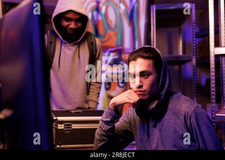 Two young criminals hacking database while using illegal malicious software on computer. Asian and african american hackers cracking password and programming malware together Stock Photo