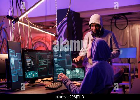 Hackers working together and coding ransomware on multiple computer screens. Internet thieves team planning cyberattack to stealing information from database server in hideout Stock Photo