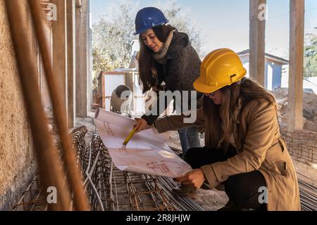 Women architects working in team, measuring in construction site with blueprint in hand.Female construction engineer and architect with hard hat weari Stock Photo