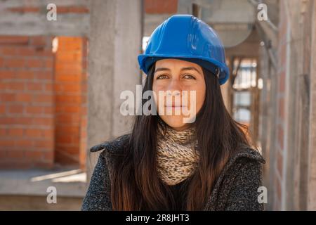 Portrait of an engineer on a construction site looking at the camera. Female construction site manager in blue hard hat. Successful and confident arch Stock Photo