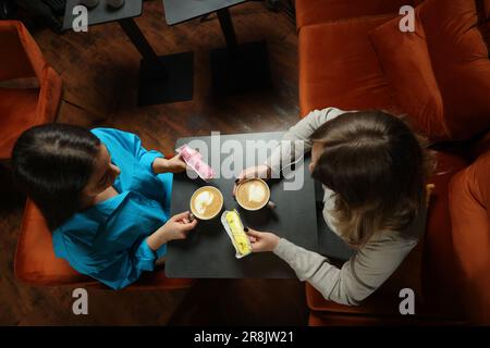 Young women with coffee and eclairs spending time together in cafe, above view Stock Photo