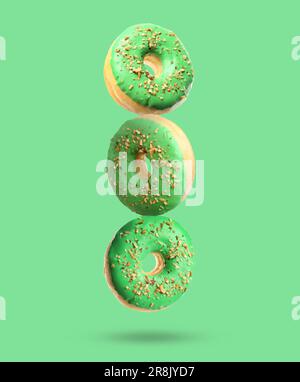 Tasty donuts with sprinkles falling on light green background Stock Photo