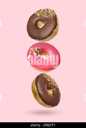 Different tasty donuts falling on pastel pink background Stock Photo