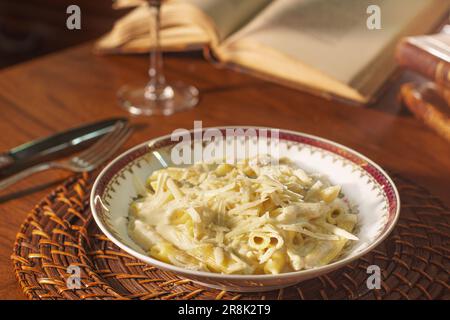 Gorgeous dish of penne with white cheese sauce. In the  background old books Stock Photo